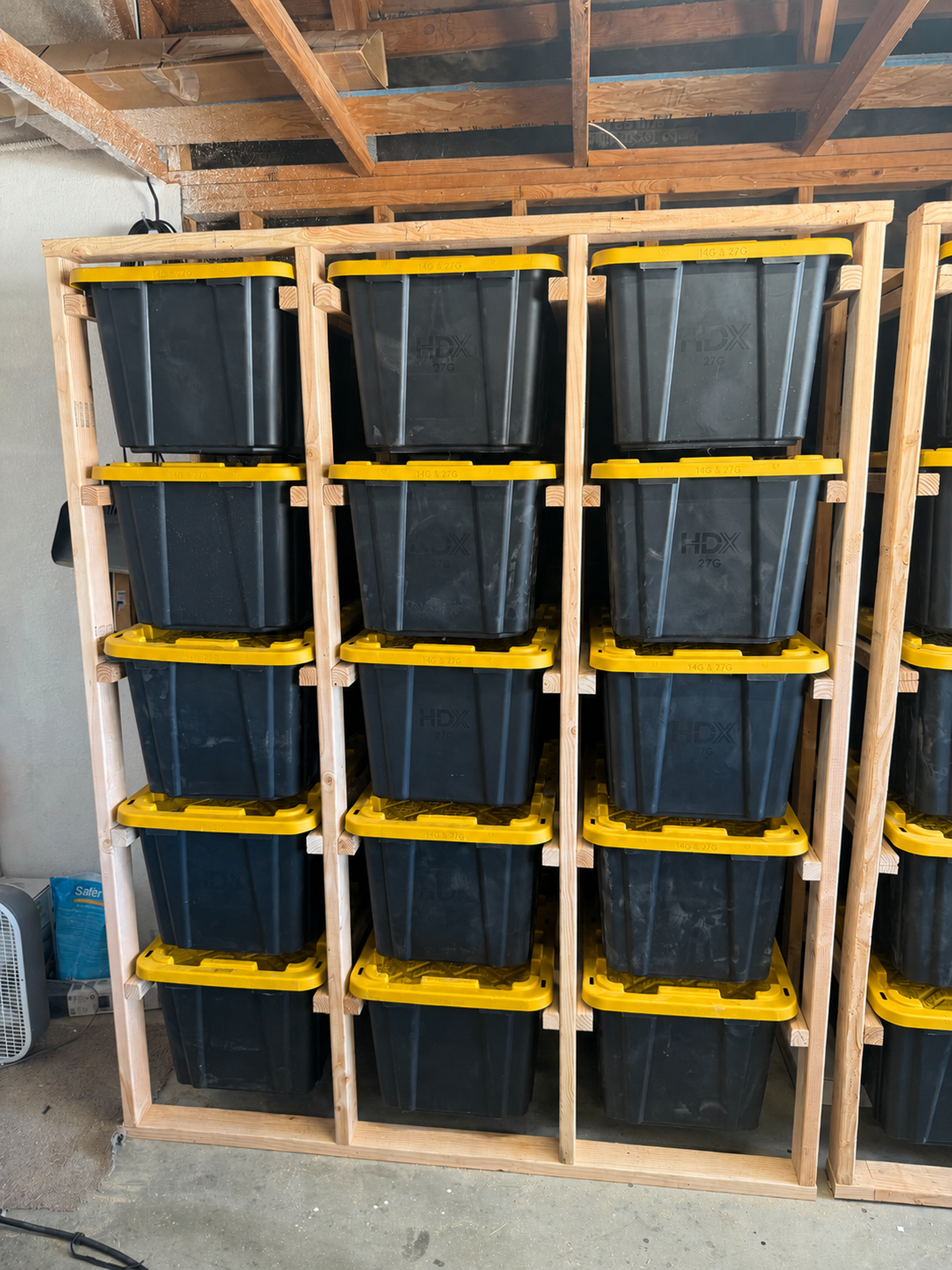 Wooden garage rack holding fifteen black totes with yellow lids